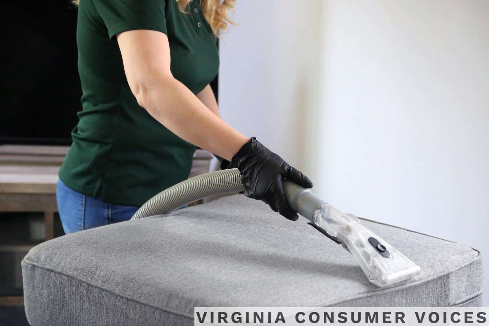 a woman in a green shirt and black gloves vacuuming a gray ottoman